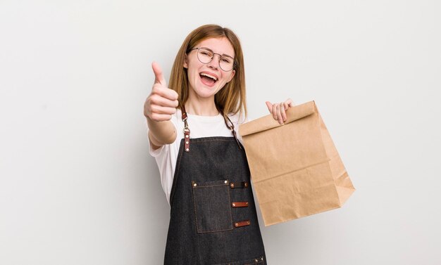Redhead pretty girl feeling proudsmiling positively with thumbs up take away employee