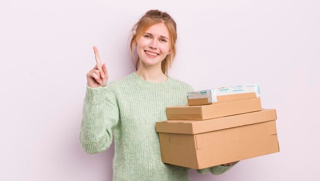 Redhead pretty girl smiling and looking friendly showing number one shipping boxes concept