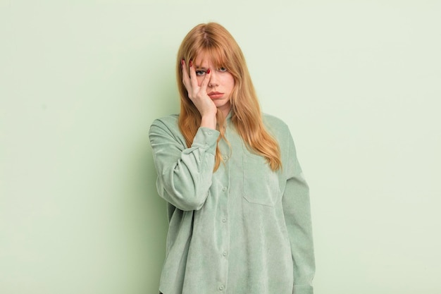 Redhead pretty woman feeling bored frustrated and sleepy after a tiresome dull and tedious task holding face with hand