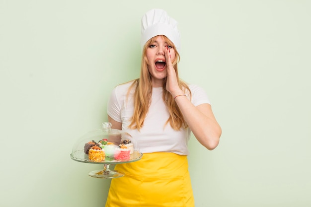 Redhead pretty woman feeling happy,giving a big shout out with hands next to mouth. home made cakes concept