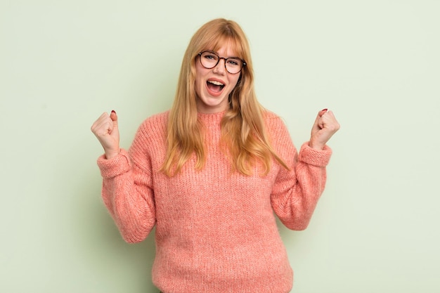 Foto donna graziosa della testarossa che sembra estremamente felice e sorpresa che celebra il successo gridando e saltando