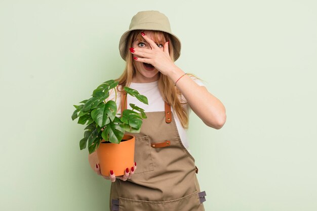 Redhead pretty woman looking shocked, scared or terrified, covering face with hand. gardener concept