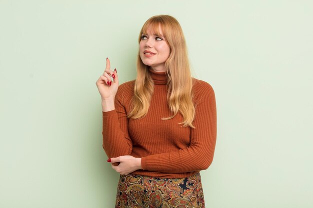 Redhead pretty woman smiling happily and looking sideways wondering thinking or having an idea