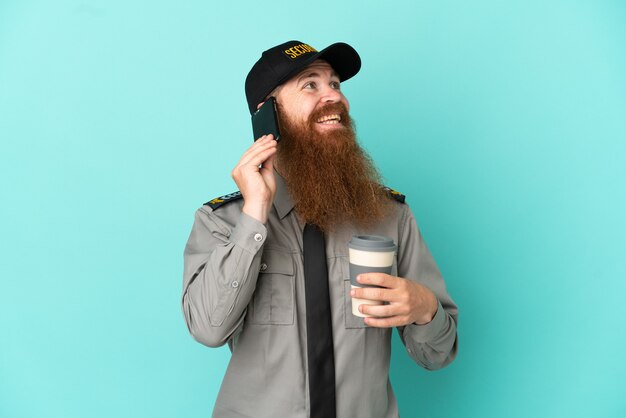 Redhead security man isolated on white background holding coffee to take away and a mobile