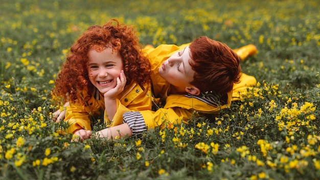 Redhead siblings in yellow raincoats on meadow