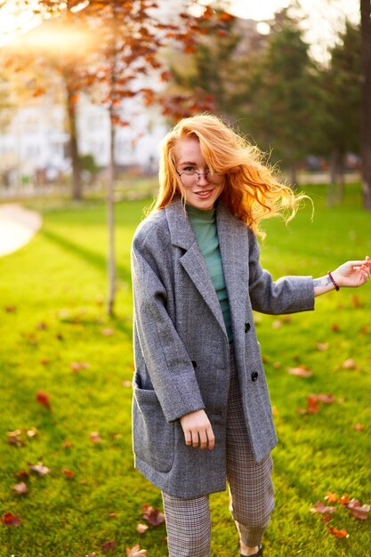 Redhead smiling pretty woman walking in park on sunny autumn day elegant female poses in stylish