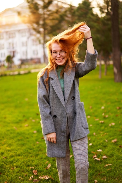 Redhead smiling pretty woman walking in park on sunny autumn day elegant female poses in stylish