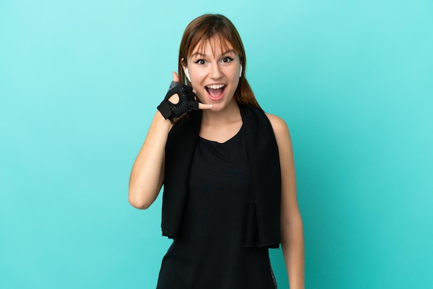 Redhead sport girl isolated on blue background making phone gesture Call me back sign