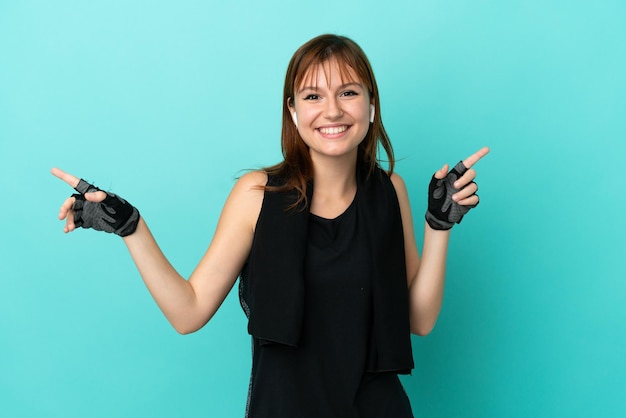 Redhead sport girl isolated on blue background pointing finger to the laterals and happy