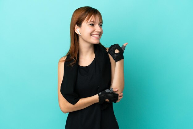 Redhead sport girl isolated on blue background pointing to the side to present a product