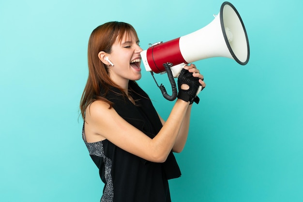 Redhead sport girl isolated on blue background shouting through a megaphone