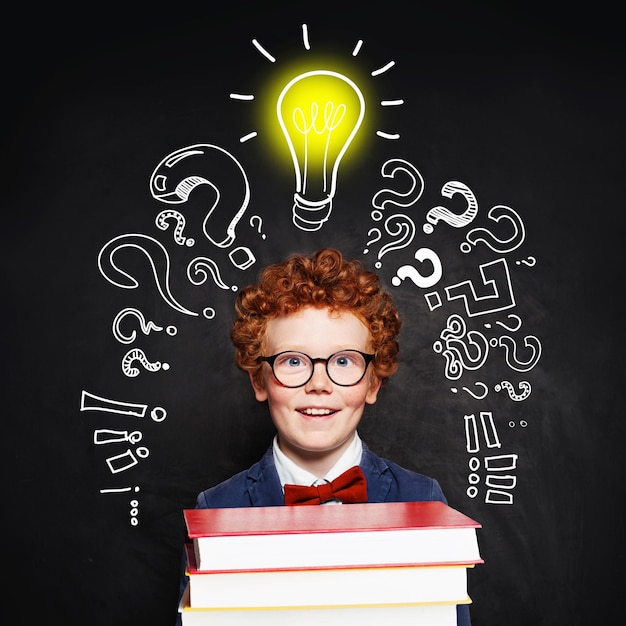 Redhead student child with lightbulb on blackboard background Idea concept