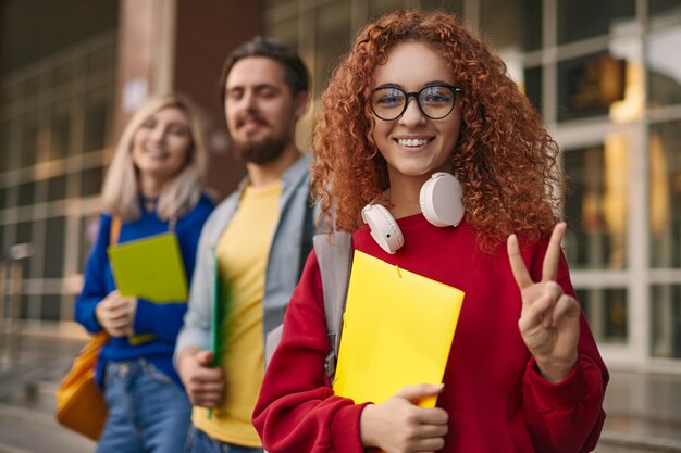 友人の近くで V サインを身振りで示す赤毛の学生