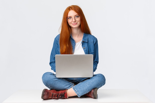 redhead student sitting with legs crossed on floor using laptop