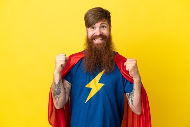 Redhead Super Hero man isolated on yellow background celebrating a victory in winner position