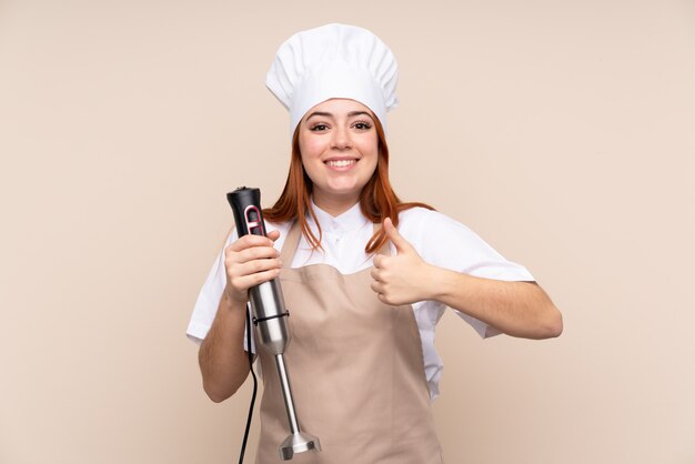 Redhead teenager girl using hand blender over with thumbs up because something good has happened