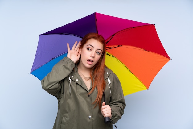 何かを聞いて傘を保持している赤毛の10代女性