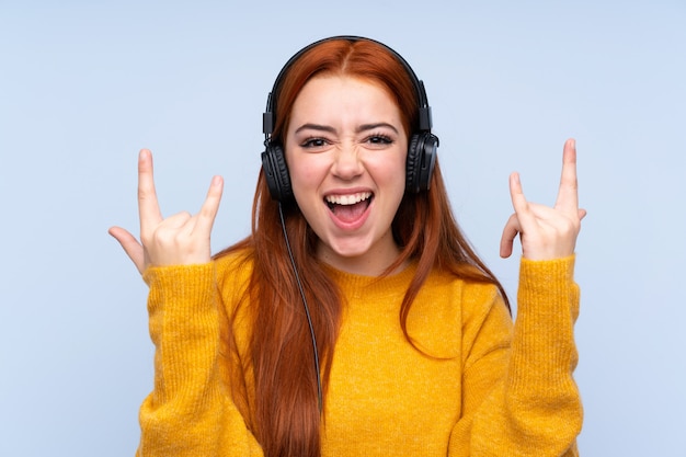 Donna dell'adolescente di redhead che ascolta la musica che fa gesto di roccia