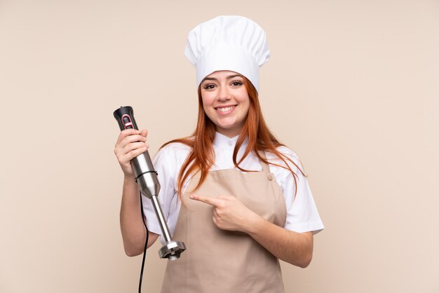 Redhead teenager woman using hand blender and pointing it