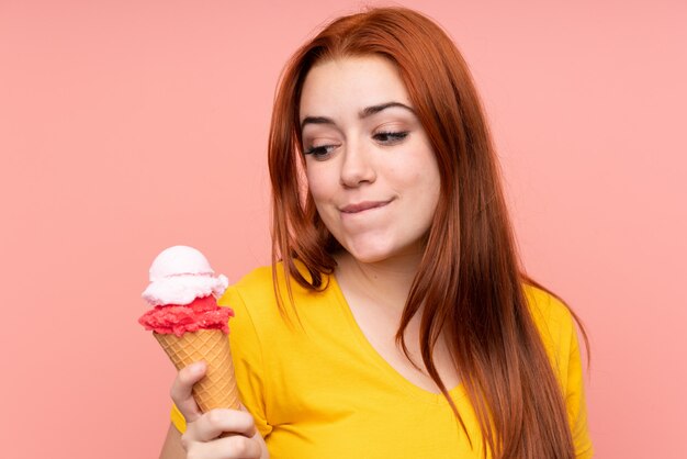 Redhead teenager woman with a cornet ice cream over isolated wall