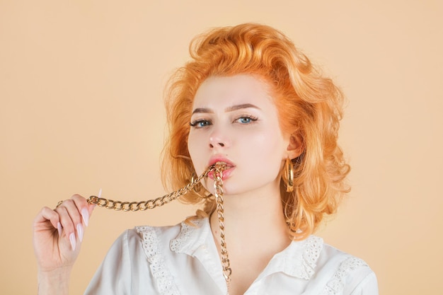 Redhead woman close up portrait with golden chain in mouth