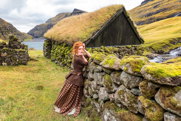 돌담 Saksun 마을 Streymoy Faroe Islands 근처에 머물고있는 빨간 머리 여자 코스프레