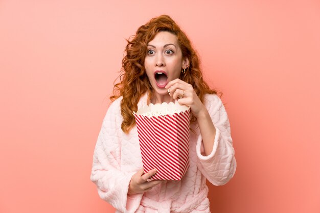 Redhead woman in dressing gown eating popcorns