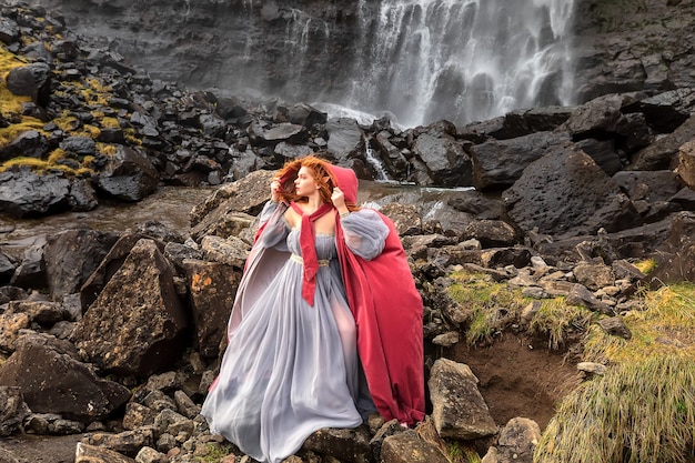 A redhead woman elf in fantasy fashioned clothes stays near Fossa Waterfall. Faroe Islands