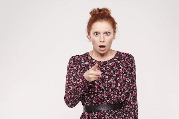 Redhead woman having surprised shocked looks pointing finger at camera