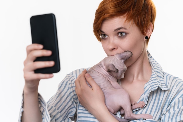 Redhead woman holding and kissing kitten taking selfie self portrait photos on smartphone