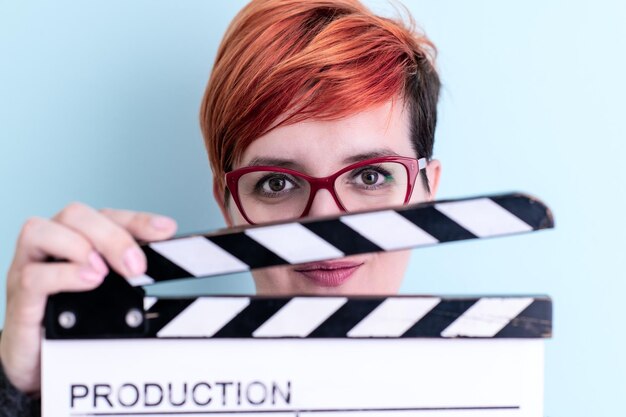 redhead woman holding movie clapper against cyan background cinema concept