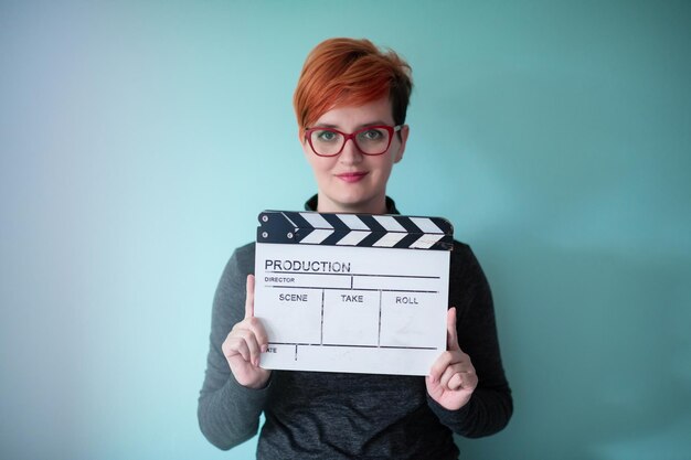 redhead woman holding movie clapper against cyan background  cinema concept