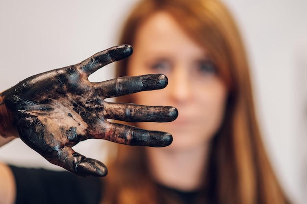 Foto pittore di donna rossa che mostra la mano colorata in vernice nera