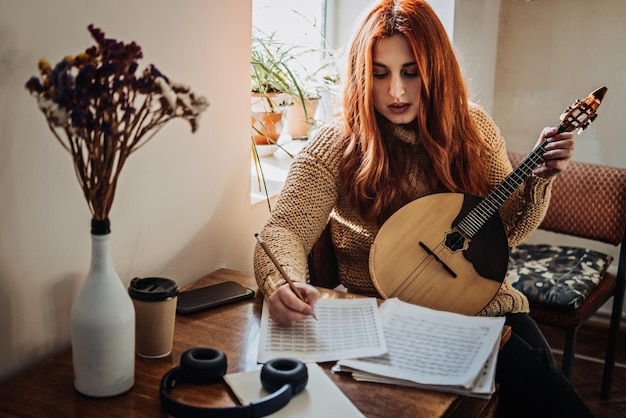 Redhead woman playing acoustic domra folk musical instrument and looking into note young woman