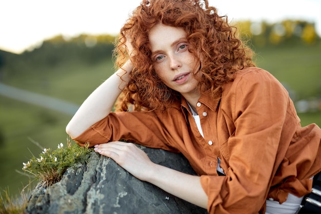 リラックスして自然に横たわっている赤毛の女性。休んでいる赤い髪の女性。山で。魅力的な白人女性は夢のようなロマンチックに見えます。田舎、田舎で屋外で休暇を過ごす