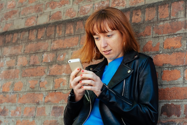 Donna della testarossa che invia messaggio con lo smartphone.