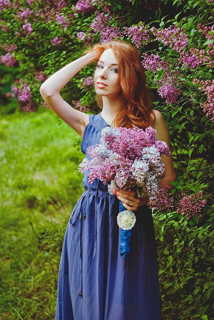 そばかすのある春の庭の赤毛の女性。紫の花が咲いています。ライラックの花束。春の季節