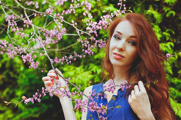redhead woman in spring garden with freckles. blooming purple flowers. Lilacs bouquet. Spring season