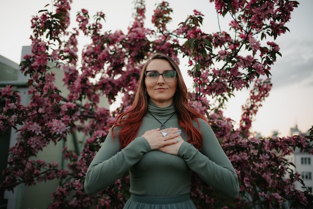 A redhead woman with flowering sakura in the background at sunset