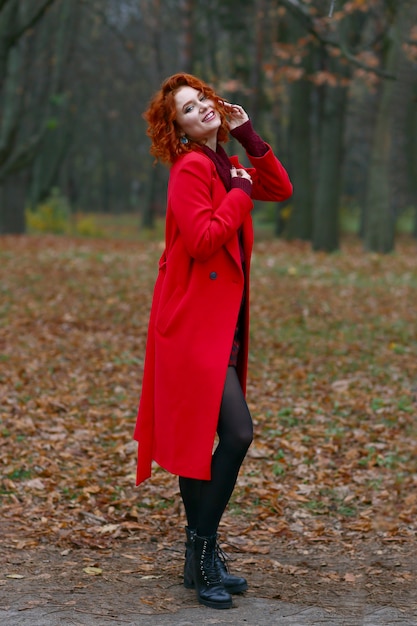 Foto donna rossa con i capelli in cappotto rosso su sfondo autunnale.