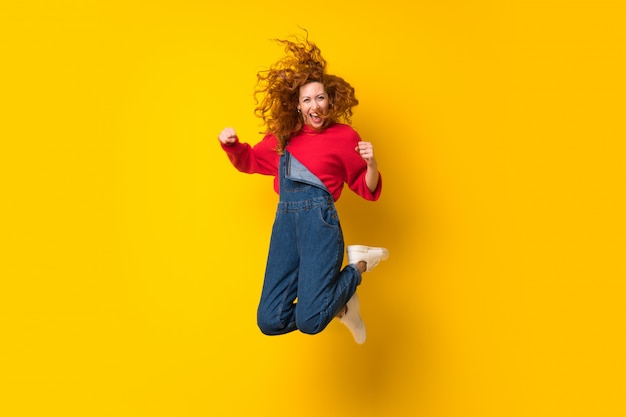 Фото Рыжая женщина с комбинезоном, перепрыгивая через желтую изолированную стену