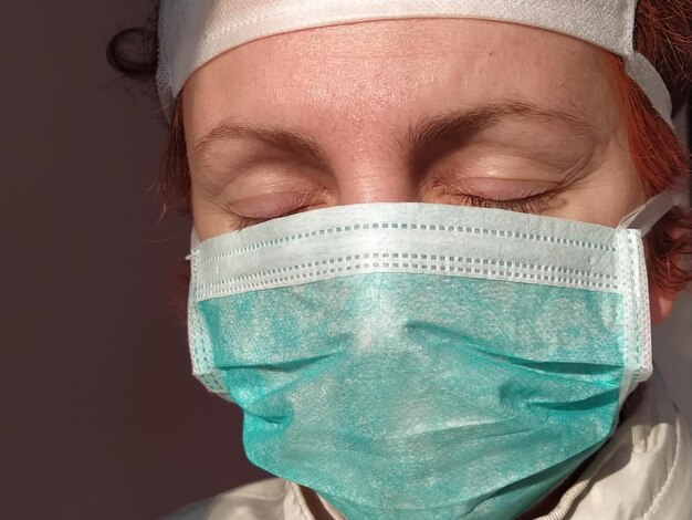 緑色の保護用サージカルマスクを着けた病気で疲れた目をした赤毛の女性 目を閉じた