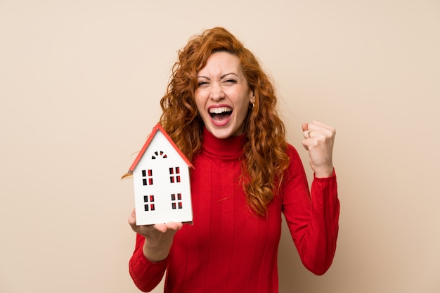 Redhead woman with turtleneck sweater holding a little house