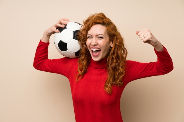 Foto donna rossa con maglione dolcevita in possesso di un pallone da calcio