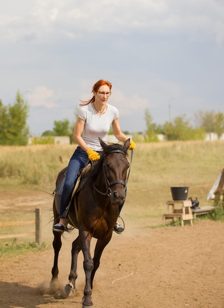 A redhead woman in yellow gloves riding a horse on the field