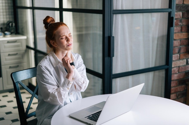 Redhead giovane donna d'affari che ha dolore al polso durante il lavoro al computer portatile mentre è seduto alla scrivania