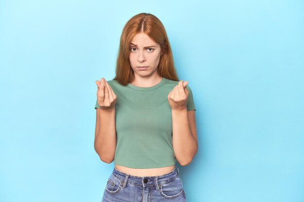그녀가 돈이 없다는 것을 보여주는 파란색 배경에 빨간 머리 젊은 여자