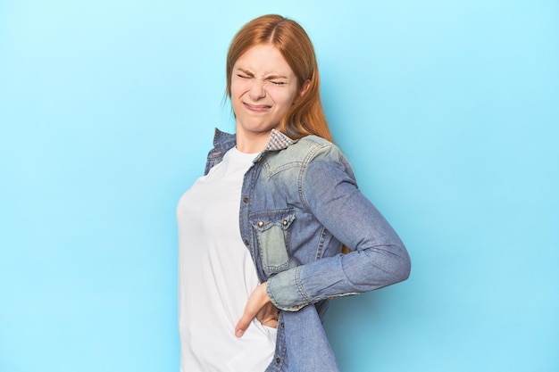 Redhead young woman on blue background suffering a back pain