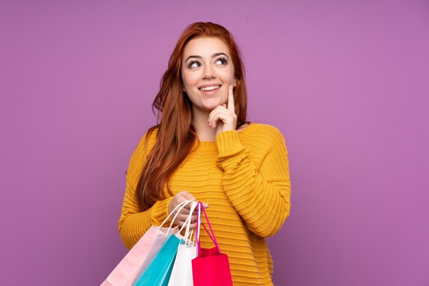 Redhead young woman holding shopping bags and thinking