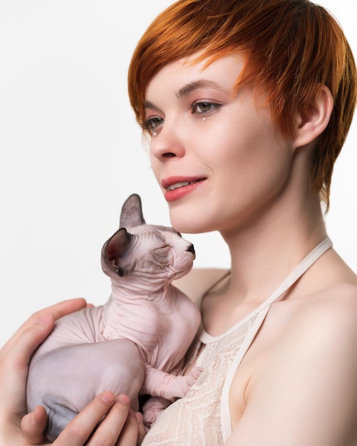 Redhead young woman hugging sleeping kitten to her chest and looking away Portrait of pretty woman